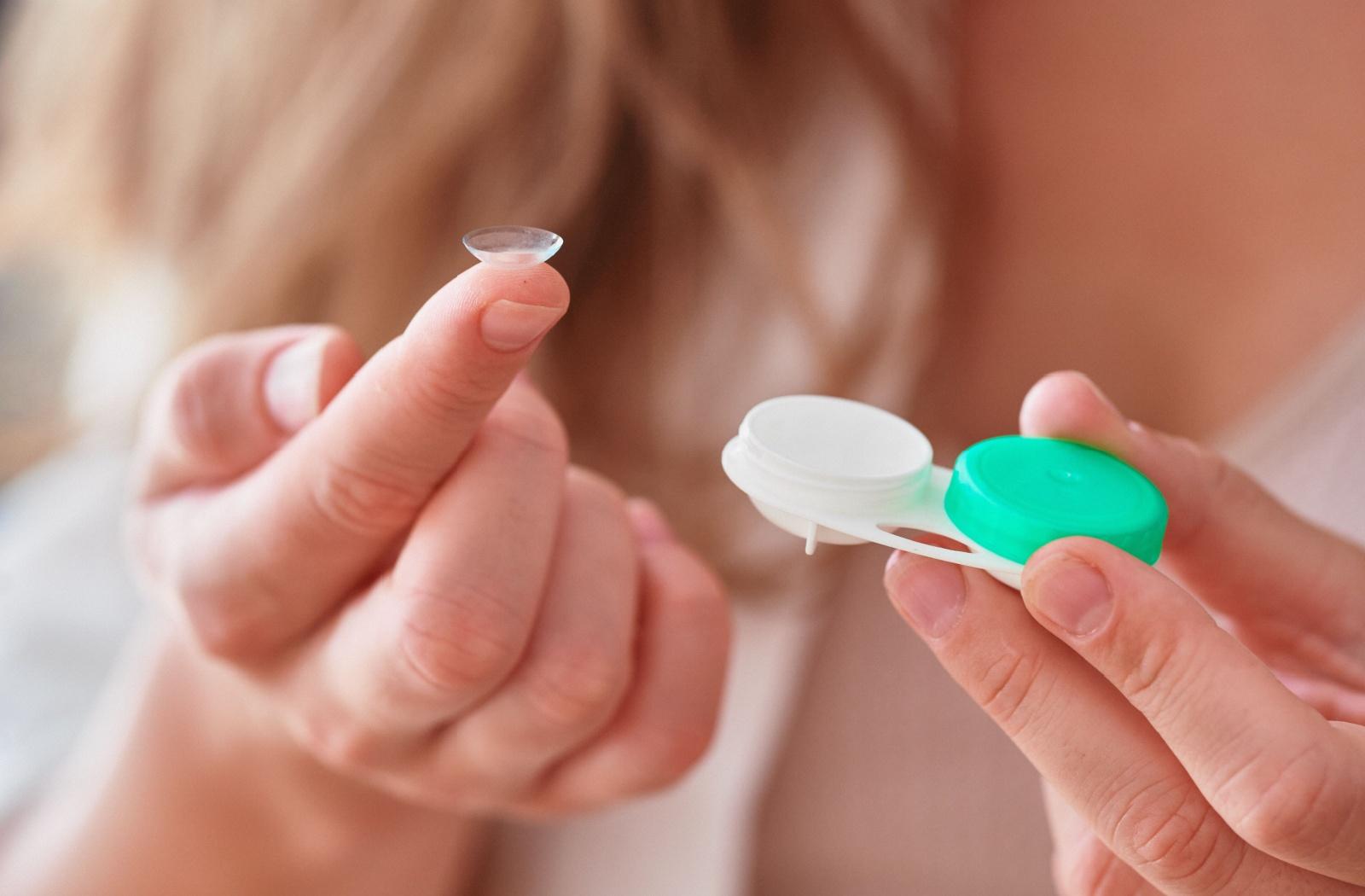Person holding a soft contact lens on their fingertip beside a contact lens case.